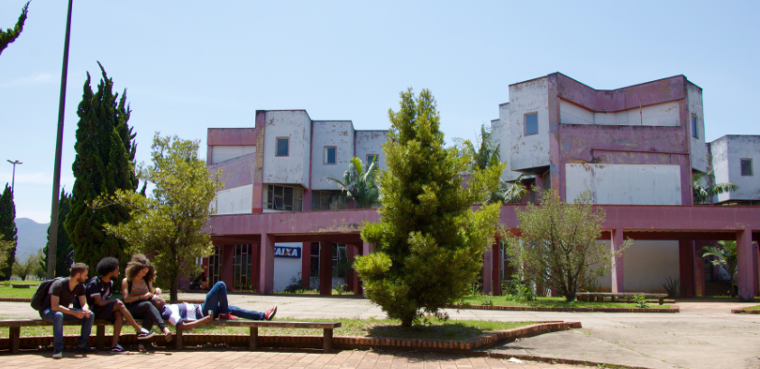Foto aberta do campus, com o Centro de Convergência ao fundo e, no primeiro plano, estudantes sentados conversando